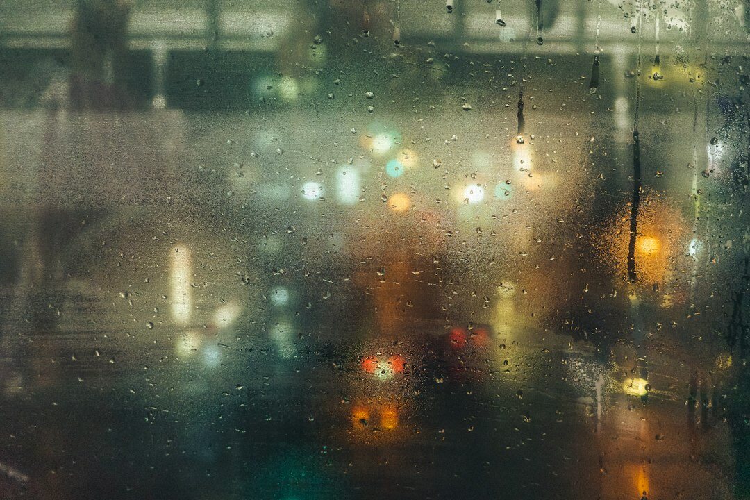 Rain drops on a window overlooking a dim city street at night