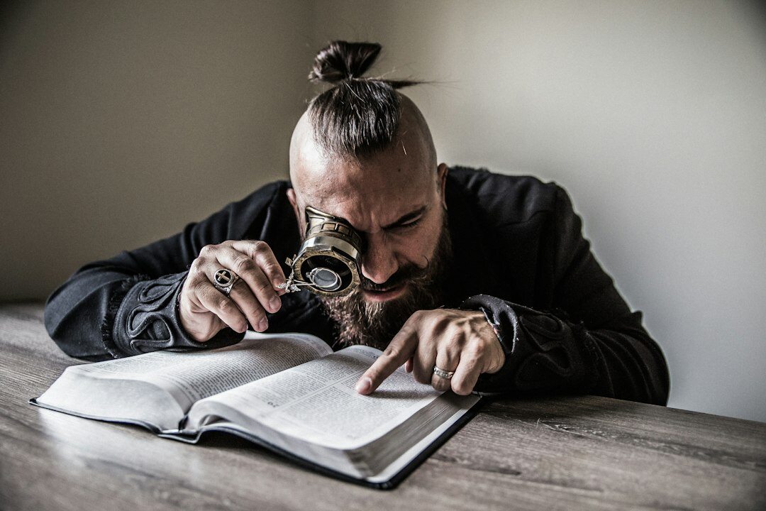 Man reading an old book by lamplight with a magnifying glass on the desk